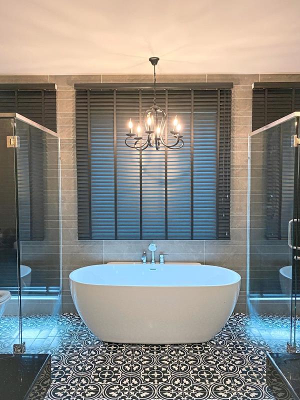 Timber blinds, a black chandelier and patterned floor tiles complement the standalone bathtub in the master bathroom.
