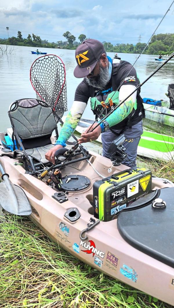 A kayak fisher placing his fishing rods on the right side of his kayak before boarding it from the left.