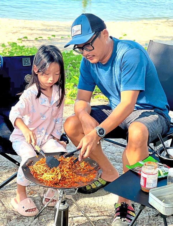 Little Avryl Tan, six, stirring up some spaghetti bolognese with minced meat and parmesan cheese on a camp stove’s griddle by the sea under the guidance of the writer.