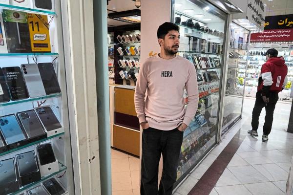 A cellphone vendor working at her shop while another waits outside his in downtown Teheran, Iran. — AP