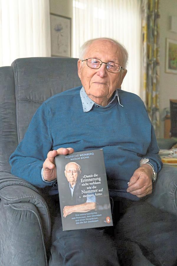 Albrecht Weinberg in his flat in East Frisia, Germany, holding his book.