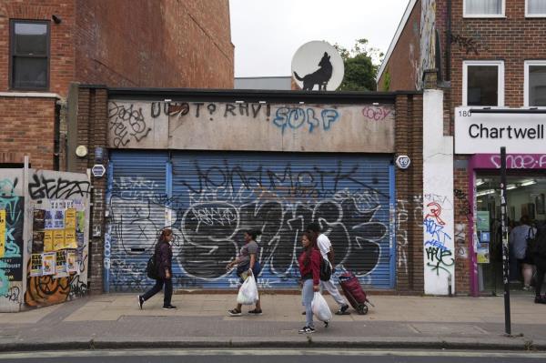 People walk past a new artwork depicting a howling wolf unveiled by Banksy, painted on a satellite dish placed on a shop roof in Peckham, south Lo<em></em>ndon on Aug 8. Photo: AP 
