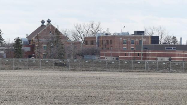 Exterior of a large, brown brick building surrounded by chain-link fencing