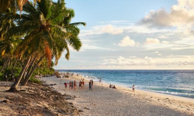 People walk along a palm-fringed sandy beach