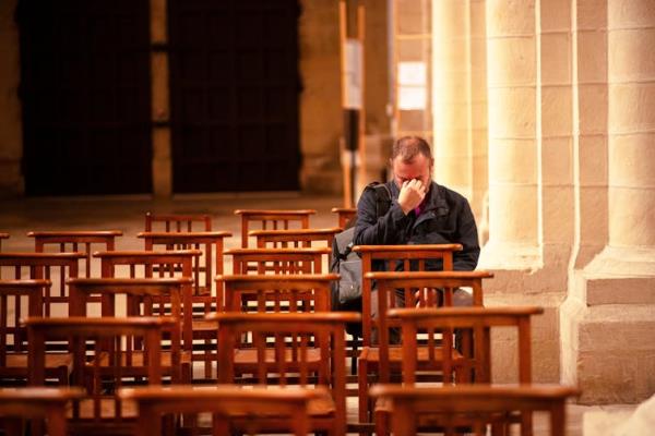 A lo<em></em>nely man sitting in a row of chairs in a church with his head in his hands