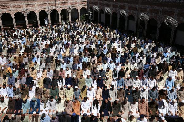 Overhead view of a large crowd of Muslim men gathering in a square for prayer, kneeling side by side in rows