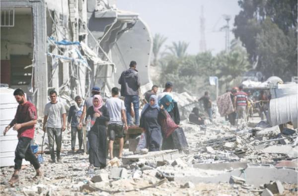  PALESTINIANS carry their belo<em></em>ngings salvaged from the debris following Israeli strikes in eastern Deir Al Balah, central Gaza Strip, on Thursday.—AFP 
