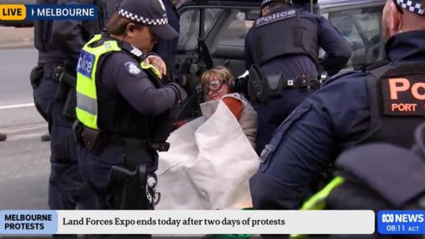 An anti-war protester has cemented herself to a car in an attempt to disrupt a weapons expo in Melbourne. Picture: ABC