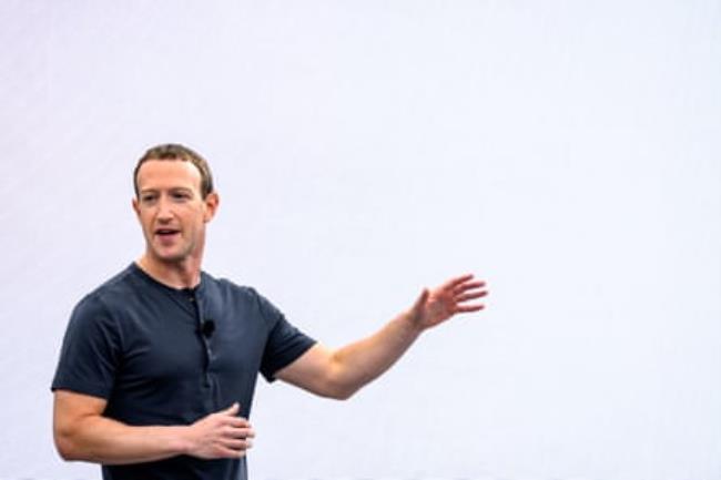 Mark Zuckerberg, wearing a navy butto<em></em>ned T-shirt, gestures while speaking on stage