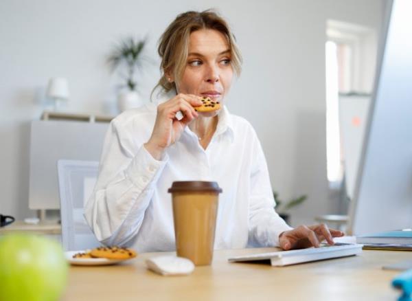 woman eating chocolate chip coo<em></em>kie, mindless snacking while working