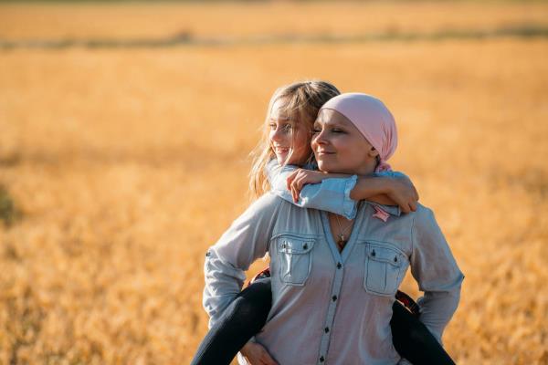 A woman with cancer carrying her daughter in a wheat field.
