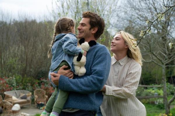 Andrew Garfield, center, as Tobias holding their daughter, and Florence Pugh, right, as Almut in a scene from We Live In Time