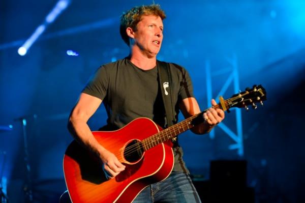 James Blunt performs on stage, playing guitar. He wears black tshirt and jeans.