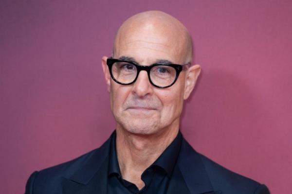 Stanley Tucci smiles for a photo against purple background