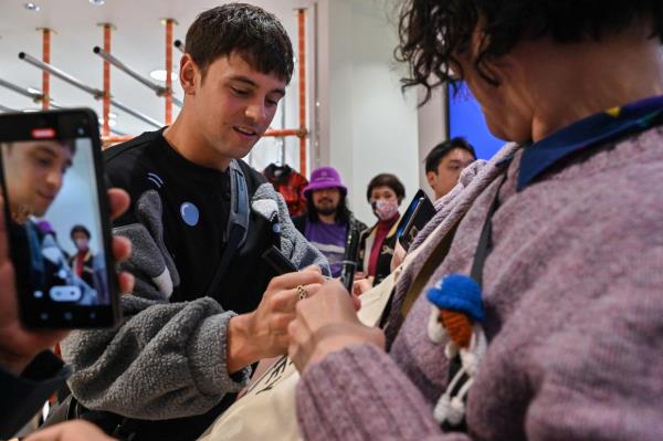 Retired British Olympic diving champion Tom Daley (L) signs an autograph for fans as he arrives at a new exhibition showcasing knitting creations he has made since taking up the craft in 2020.