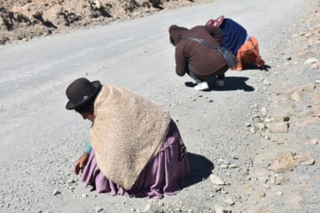 Three people crouch on a road looking at the ground