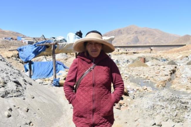 A woman stands in front of a makeshift shelter