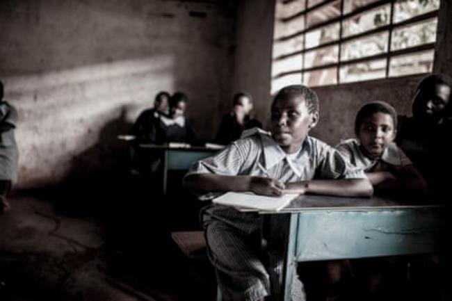Girls in school uniform sit at desks in a simple classroom