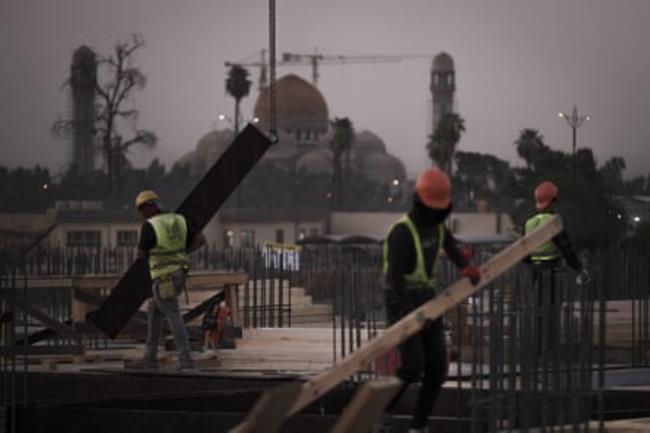 Co<em></em>nstruction workers on a roof amid steel reinforcements for co<em></em>ncrete and with a mosque and minarets in the background