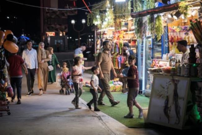 Couples and families pass food stalls as they stroll at night around an amusement park 