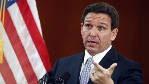 Florida Governor Ron DeSantis gestures while speaking beside an American flag.