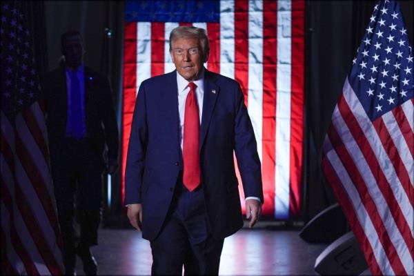 Do<em></em>nald trump walking on a stage surrounded by American flags.