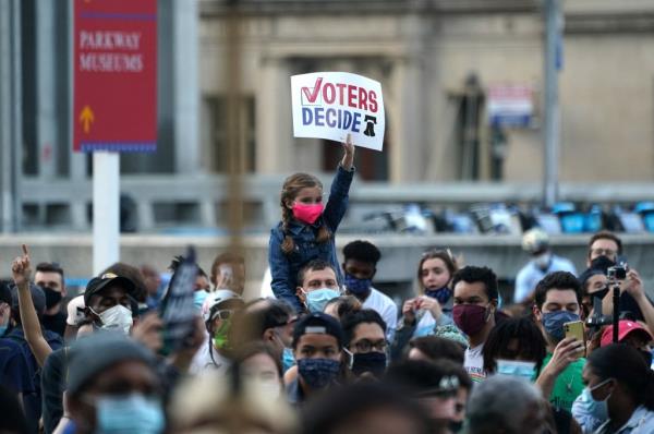 A young supporter holds a sign as people celebrate outside City Hall after Joe Biden was declared winner of the 2020 presidential election.