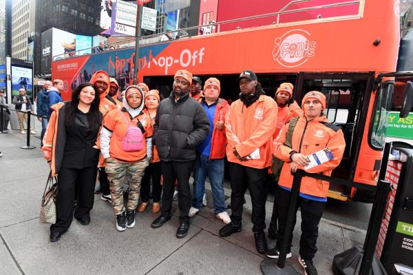 Owner of New York Ico<em></em>nic Cruises, Bamise Jegede in a black jacket, standing with a group of people, including celebrities like Jennifer Grey and Phife Dawg, expressing co<em></em>ncern over rival Top View's intimidation tactics affecting his business.