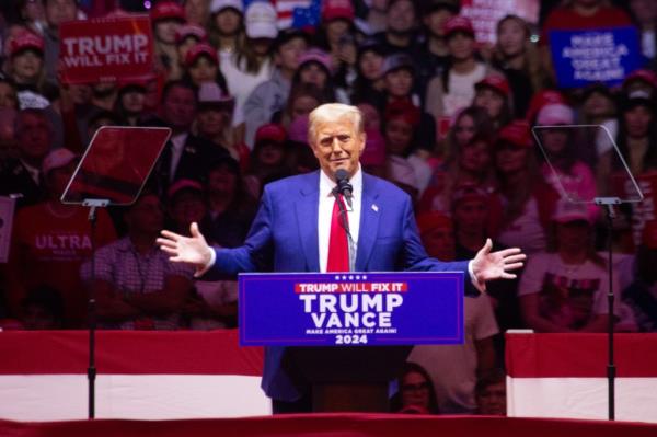 Trump opens his arms speaking behind a podium.