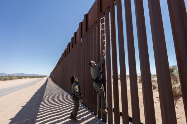 Border Patrol agents scale the border wall to try to dislodge a ladder placed there by cartel smugglers.