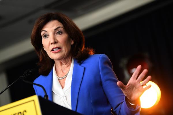 NY Governor Kathy Hochul in a blue suit, signing a bill into law, and speaking into a microphone