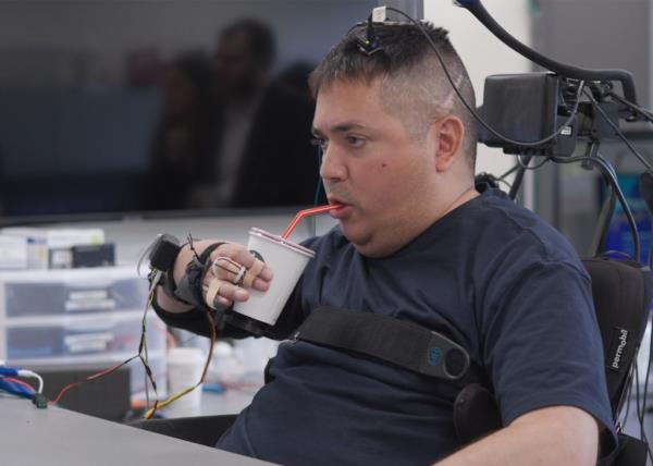 Keith Thomas, a man living with paralysis, successfully grasping, lifting, and drinking from a cup following a clinical trial