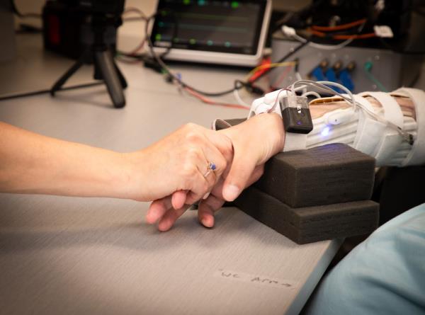 A paralyzed man experiencing sensations in his arm and hand due to a system of brain implants and artificial intelligence, making him able to hold a hand on a table.