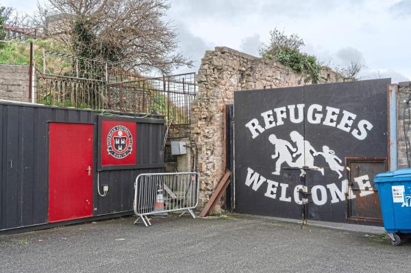 A ‘Refugees Welcome’ sign is painted on a gate at a side entrance to Dalymount Park stadium. Murals supporting various causes forming the stadium’s backdrop. The approach is not universally popular. — ?2024 The New York Times Company