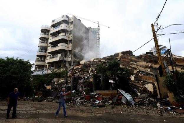 Two men walk past a flattened co<em></em>ndo building.
