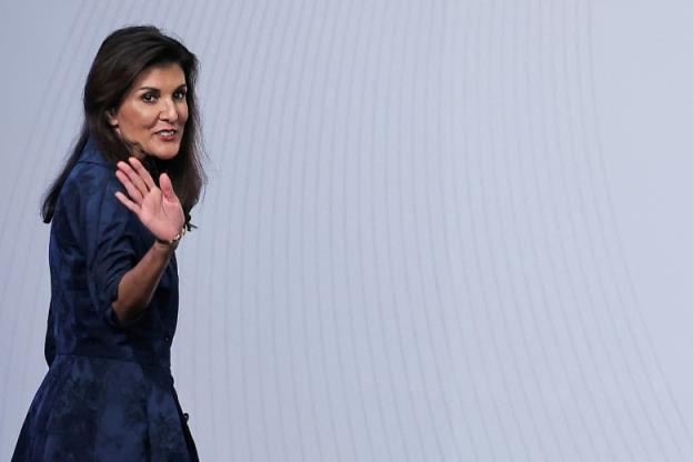 A woman in a blue dress waves as she walks.