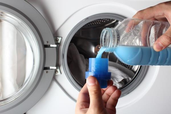 Close up of someone pouring blue fabric softener in the washing machine