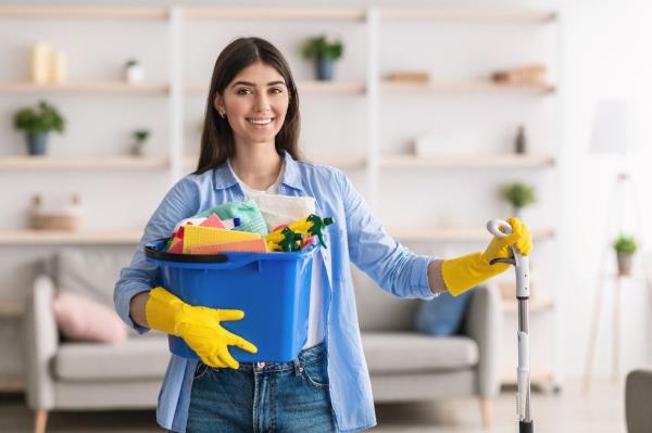 Smiling woman holding bucket with cleaning supplies and mop