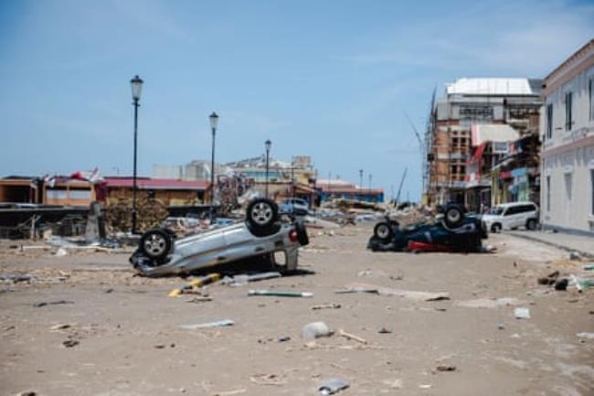 Two upturned cars in a street strewn with debris. Damaged buildings are also visible