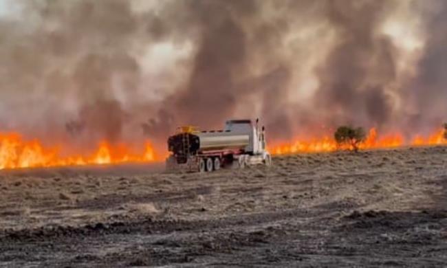 A vehicle in a field as fires burn on horizon
