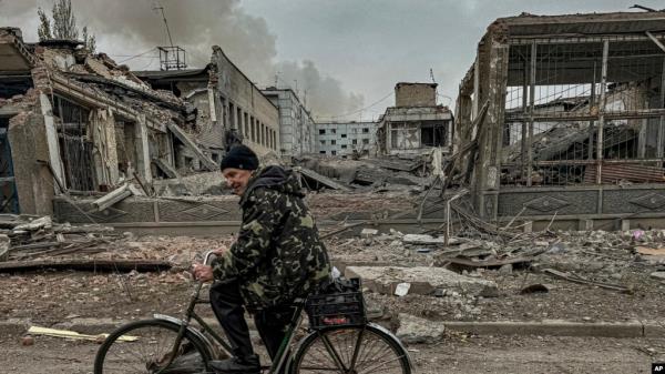 FILE - A man rides on a bike in front of the mail office which was destroyed by a Russian airstrike in Kurakhove, Do<em></em>netsk region, Ukraine, on Nov. 7, 2024.