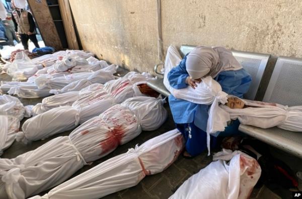 FILE - A Palestinian woman holds the body of a child as she sits by bodies of Palestinians killed by Israeli airstrikes on Jabaliya refugee camp, at the Indo<em></em>nesian hospital, northern Gaza Strip, Nov. 18, 2023.