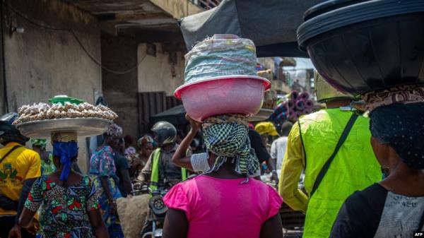 FILE - Women carry goods on their head as they walk in the Dantokpa market, one of the largest open-air market in West Africa, in Cotonou, Benin, on Feb. 29, 2024. 
