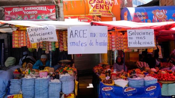 FILE - Handwritten sign with messages that read in Spanish: 'We demand solutions from the government,' 'Arce, don't starve us' and 'Solutions, not more problems' hang from vendors' stalls at a street market in La Paz, Bolivia, Oct. 21, 2024. 