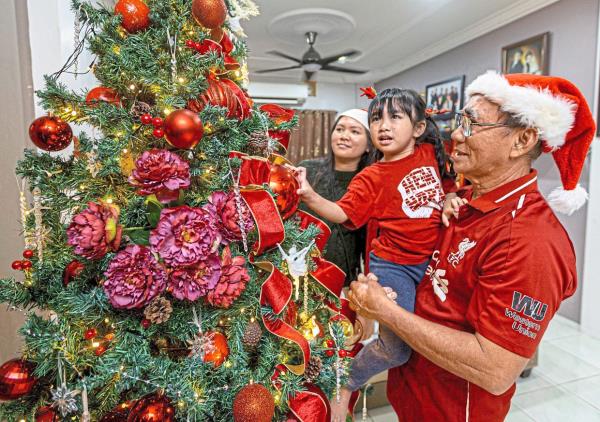 Festive fun: Edward Taji Ranti from Kampung Semaba in Kuching helping his granddaughter to hang a bauble on a Christmas tree in their home as the family gets ready to celebrate Christmas. — ZULAZHAR SHEBLEE/The Star