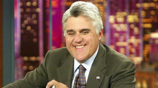 Jay Leno hosting The To<em></em>night Show at desk and smiling