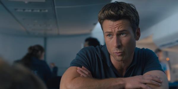 Glenn Powell as Ben looking curious on a plane in Anyone But You