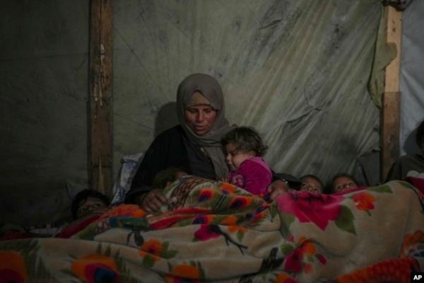 Reda Abu Zarada wraps herself and her grandchildren in blankets as they prepare to sleep in their tent at a camp in Khan Younis, Gaza Strip, Dec. 19, 2024.