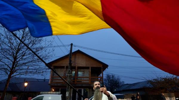 A man waves the Romanian flag outside a closed voting station after Romania's Co<em></em>nstitutional Court annulled the first round of presidential elections, in Mogosoaia on Dec. 8, 2024. The EU said on Dec. 17 it was investigating video-sharing platform TikTok regarding the election.