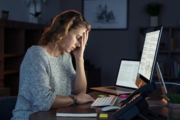 A woman sitting in front of a computer at a desk rests her head against her hand